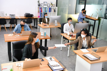Asian office workers wearing face masks working in new normal office and doing social distancing...