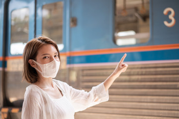 Woman in protective mask wait for the local train on platform at station.