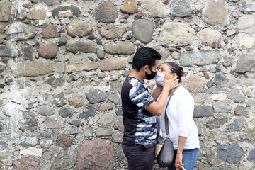 Obraz na płótnie Canvas Young Latino couple with protective face masks and stone wall in the background, new normal covid-19