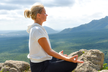 Naklejka na ściany i meble young woman meditates on a high stone mountain.