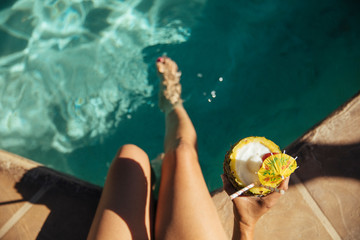 A woman holds a tropical pineapple drink poolside at a resort
