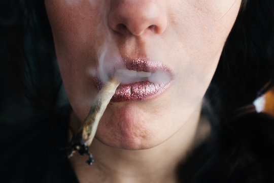 Female lips smoking self-roll weed cigarette. Close-up, lips and fume