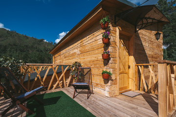 Fototapeta na wymiar Chair on Terrace near Wooden house, resort in beautiful mountains, sunny summer day