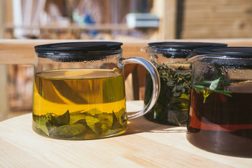 Tea made of natural herbs on wooden desk in glass decanter pot, mountains landscape on background