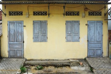 Fototapeta na wymiar Weathered wooden doors and window shutters set in a faded yellow wall in rural Southeast Asia