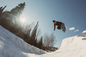 Snowboarder male jumping on quarter pipe snowboard in winter sunny day. Freestyle snowboard training