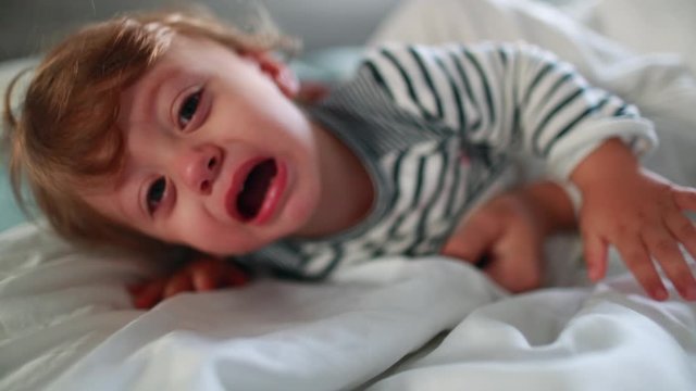 Upset baby infant having a tantum in morning bed. Angry toddler tearful child boy cries having tantrum