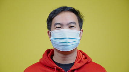 Portrait happy Asian man wear face mask to protect against Coronavirus (COVID-19) or bacteria and dust. Face Authentic close up. isolated Yellow on background. Concept Health care