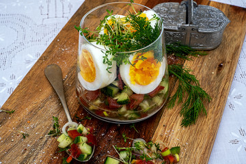 .halved boiled eggs in a glass with chopped tomatoes, cucumber and onions, dill and garden cress