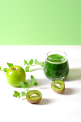 Green fruit and spinach smoothie in a glass glass with fruit and mint next to it. Healthy nutrition concept, alkaline diet, detox. Vertical orientation, copy space.