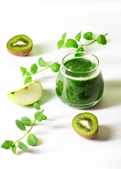 Green fruit and spinach smoothie in a glass, with apple and kiwi slices next to it. Healthy nutrition concept, alkaline diet, detox.