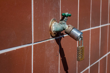  A combination lock on the end of an outdoor water faucet atached to a red grid tiled wall . The...