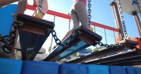 Two little  sisters have fun at the playground made in marine theme. Close up feet of girls passing the obstacle course attraction on sunny summer day .  50 fps slow motion 