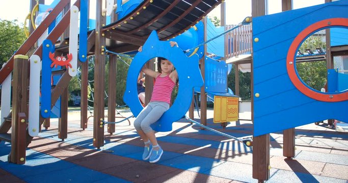 Two little pretty sisters, five and eight years old, have fun at the playground made in marine theme. Girl swinging on plastic fish-shaped construction and waving their hands and smiling