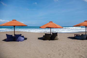 Fototapeta na wymiar Orange sun umbrellas and empty bean bags on Berawa Beach (Pantai Berawa ), Canggu, Badung, Bali, Indonesia