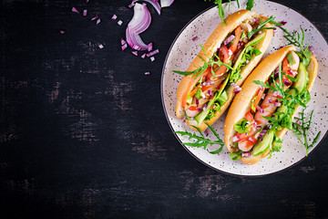 Hot dog with sausage, cucumber, tomato and red onion on dark background. Top view. Flat lay. Copy space