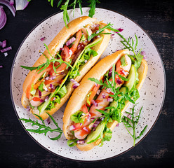 Hot dog with sausage, cucumber, tomato and red onion on dark background. Top view. Flat lay. Copy space