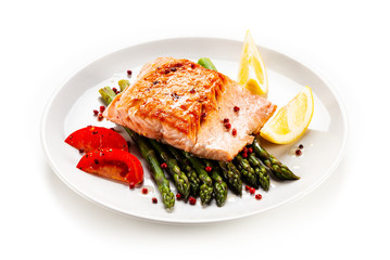 Fried salmon fillet with asparagus, lemon and tomatoes on white background

