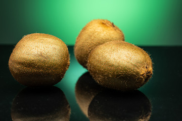 several kiwis on dark glass with green glare on green background