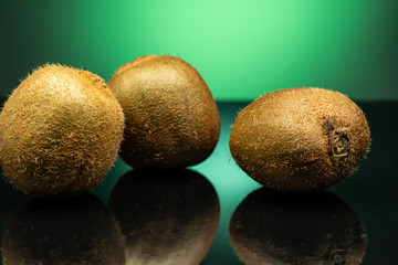 several kiwis on dark glass with green glare on green background