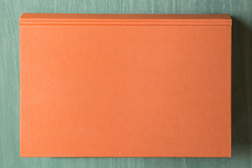 Overhead view of a large orange book on a green wooden table.