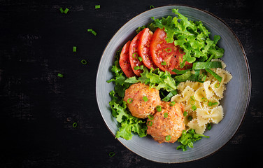 Italian pasta. Farfalle with meatballs and salad on dark background. Dinner. Top view, overhead. Slow food concept