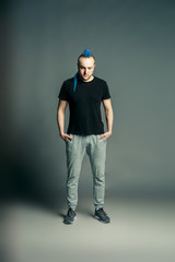 portrait of a young man with an unusual hairstyle of mohawk from blue braids in sportswear posing...