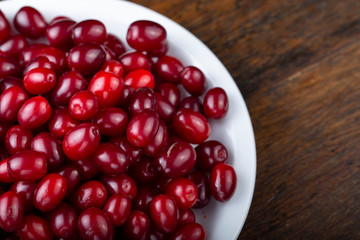 Dogwood in a white plate on a wooden background. Gathering the summer harvest.