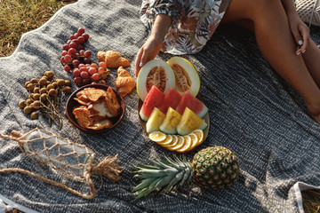 Summertime eco picnic setting on the grass with pineapple, watermelon, grapes and wine on  grey tablecloth. Top view, woman legs - Powered by Adobe