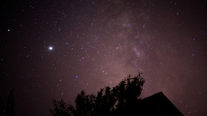 Starry night sky and the milky way against the background of a tree and the roof of a house at...