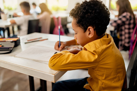 African American schoolboy writing at his desk in the classroom.