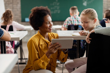 Happy black teacher and schoolgirl using digital tablet in the classroom.