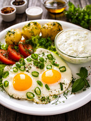 The best summer dinner - sunny side up eggs, boiled potatoes, cucumbers in yogurt  and fresh vegetables served on wooden table
