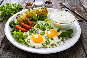 The best summer dinner - sunny side up eggs, boiled potatoes, cucumbers in yogurt  and fresh vegetables served on wooden table
