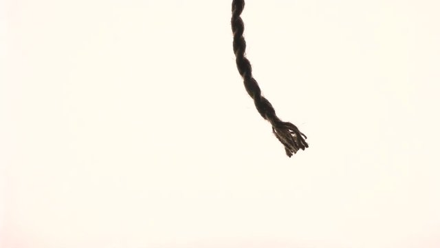 A clipped and frayed rope hangs and sways against a white background. As a symbol of something not good.