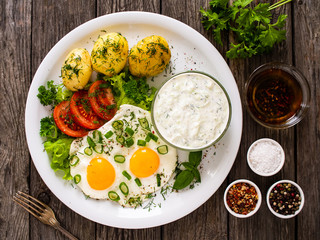 The best summer dinner - sunny side up eggs, boiled potatoes, cucumbers in yogurt  and fresh vegetables served on wooden table
