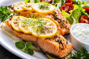Roasted salmon steaks with lemon, cream sauce and vegetable salad served on wooden table

