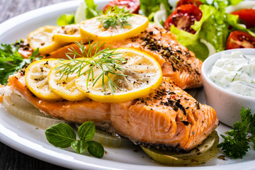 Roasted salmon steaks with lemon, cream sauce and vegetable salad served on wooden table
