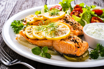 Roasted salmon steaks with lemon, cream sauce and vegetable salad served on wooden table
