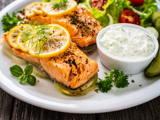 Roasted salmon steaks with lemon, cream sauce and vegetable salad served on wooden table
