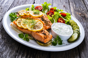 Roasted salmon steaks with lemon, cream sauce and vegetable salad served on wooden table
