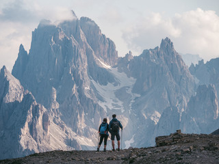 Couple of hikers standing and admiring stunning beauty of impressive jagged peaks of Cadini di misurina mountain group in Dolomites, Italy, part of Tre Cime di Levaredo national park