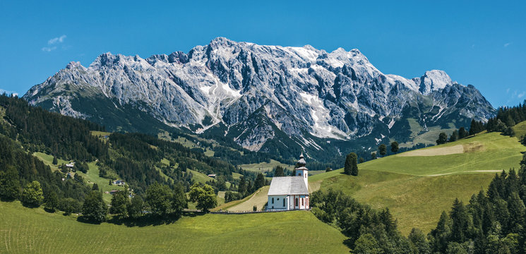Panorama of green meadows and parish church of Dienten with Hochkönig mountain on the background. Pinzgau, Salzburg, Austria.
