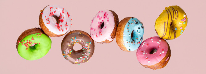 Doughnut collection with flying blue, pink, green and yellow donuts on pink background