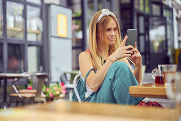 Pretty red-haired girl with freckles reading a message on smartphone in a cafe