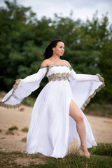 Young european woman with brown hair dressed a long white wedding dress stays near the river