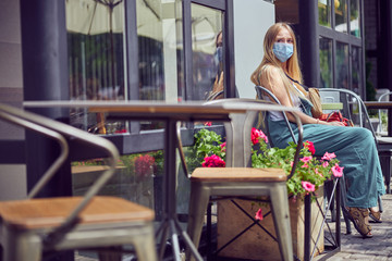 Red-haired pretty girl sitting at the table outdoors wearing a mask