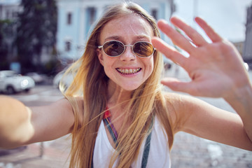 Cheerful smiling pretty girl with freckles taking a selfie outdoors