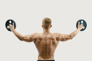 Rear view of young bodybuilder lifting weights rising hands against white background. Fit and...