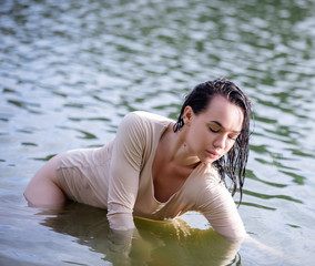 Young European woman with dark hair in wet closes posing in water 